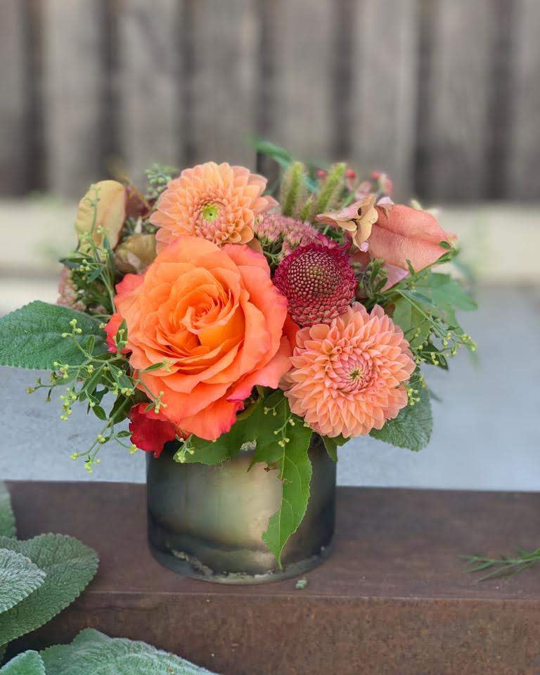 Floral arrangement with orange and pink flowers in a glass vase on a wooden surface.